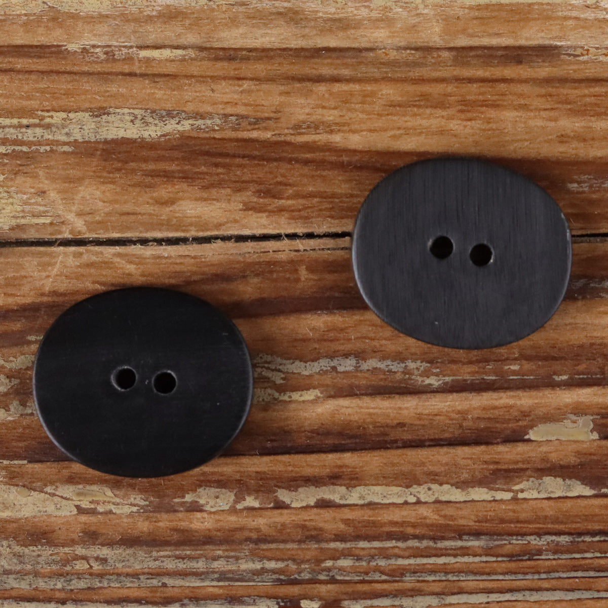 Oval two-hole horn buttons, dark grey and black with carved linear edge texture.