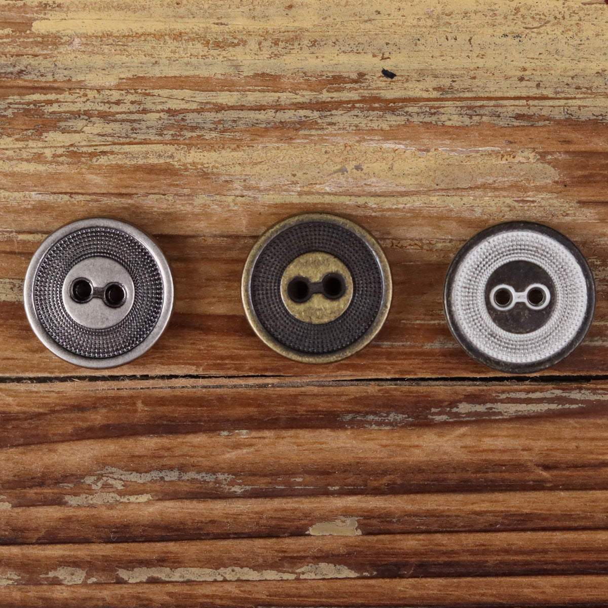 Three 2-hole metal buttons with concentric circle texture in silver, dark bronze, and bronze tones
