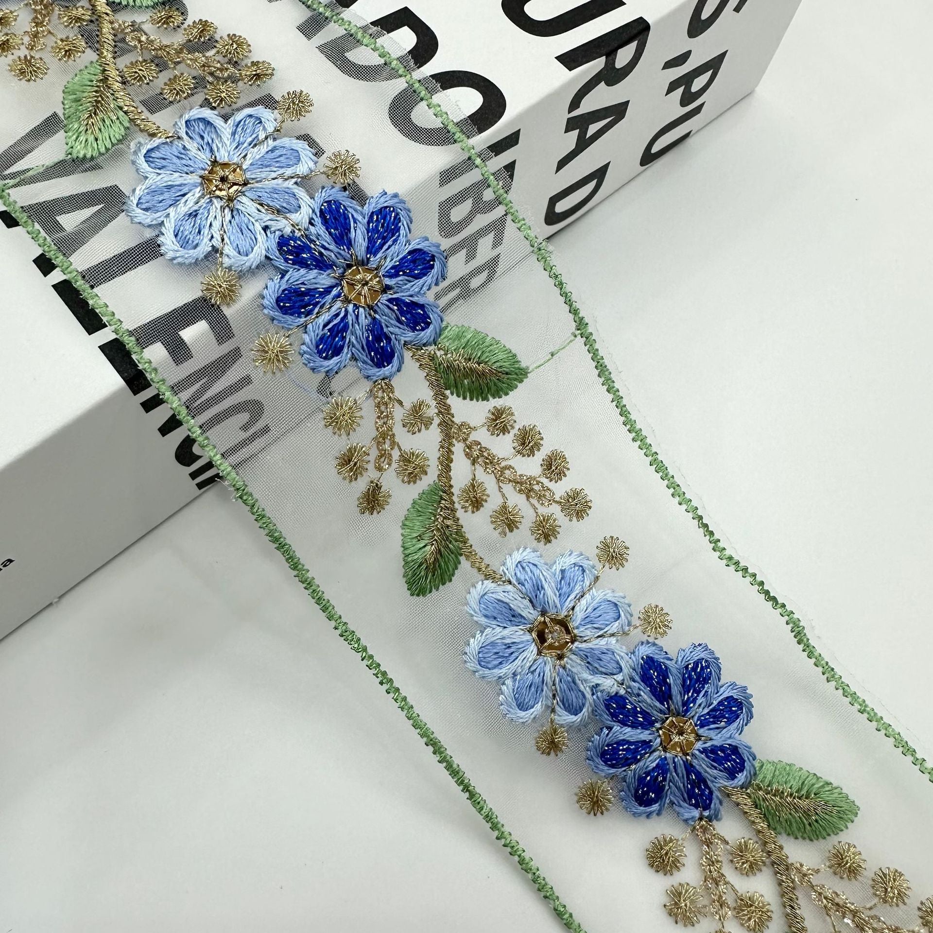 Blue embroidered organza lace trim with clustered blue flowers, gold accents and green edge