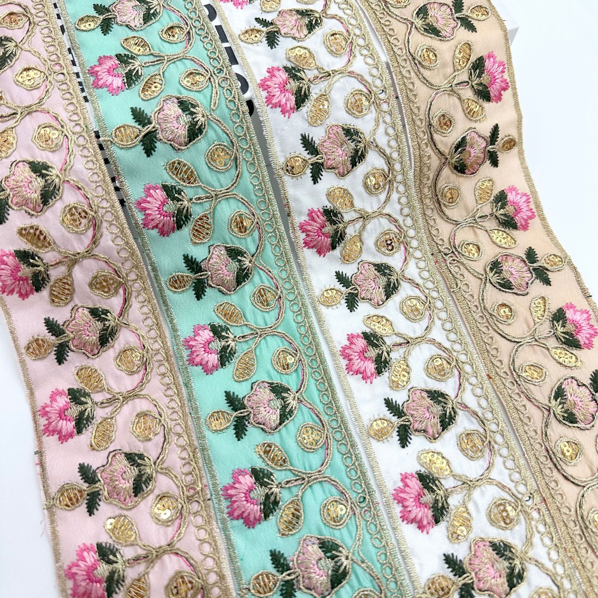 Embroidered lace trim ribbon with pink flowers, gold motifs, and teal fabric background