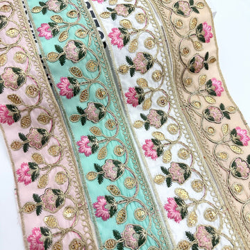 Embroidered lace trim ribbon with pink flowers, gold motifs, and teal fabric background