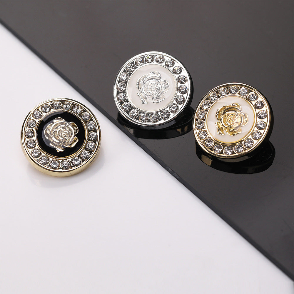 Drei runde Zierknöpfe mit Strasskranz: silber und goldfarben mit Blumenmotiv auf dunklem Grund