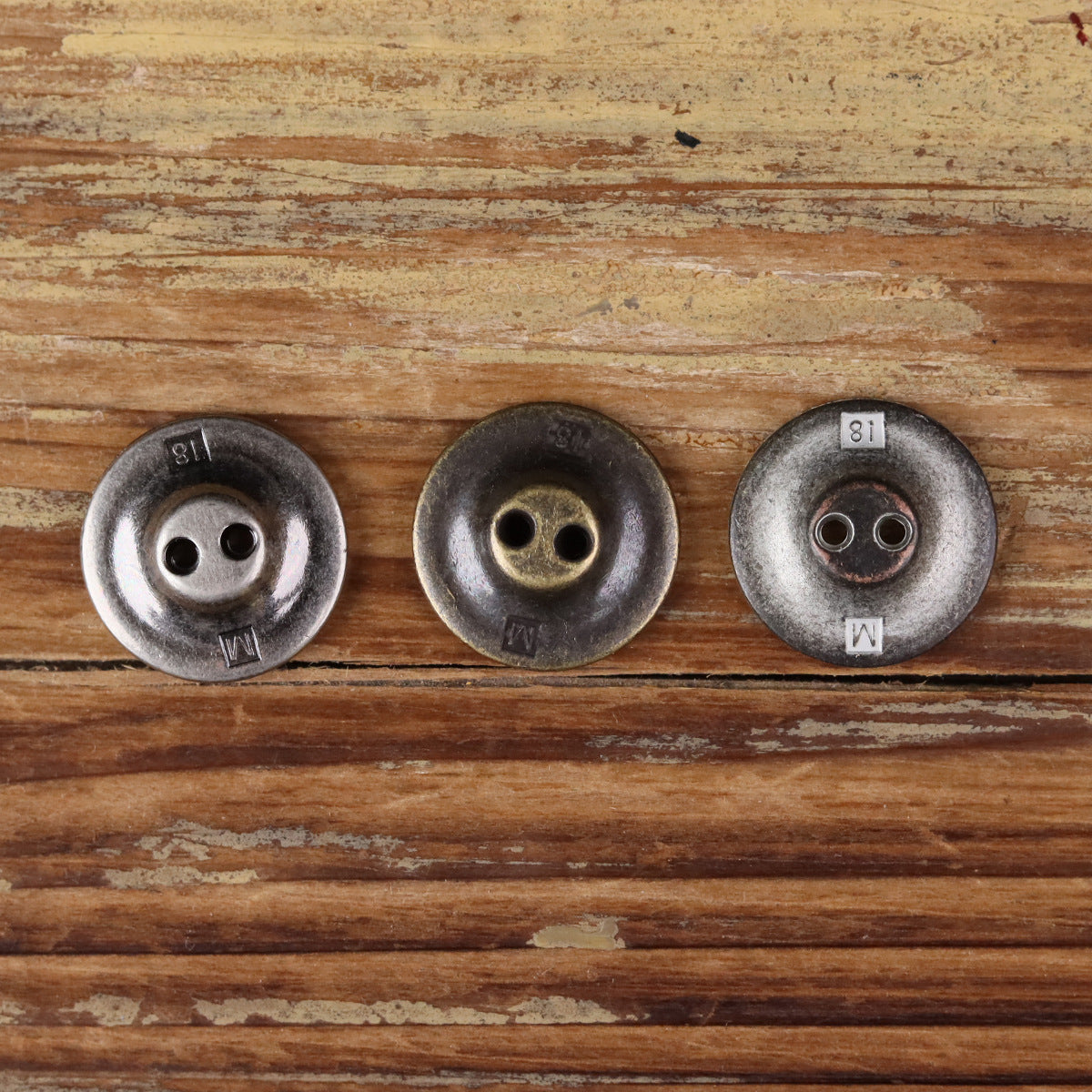 Three 2-hole metal buttons with concentric circle borders in silver, bronze, and dark finishes
