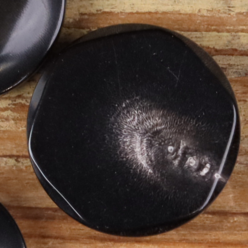 Buffalo horn button in dark color with irregular edge and hidden eye detail