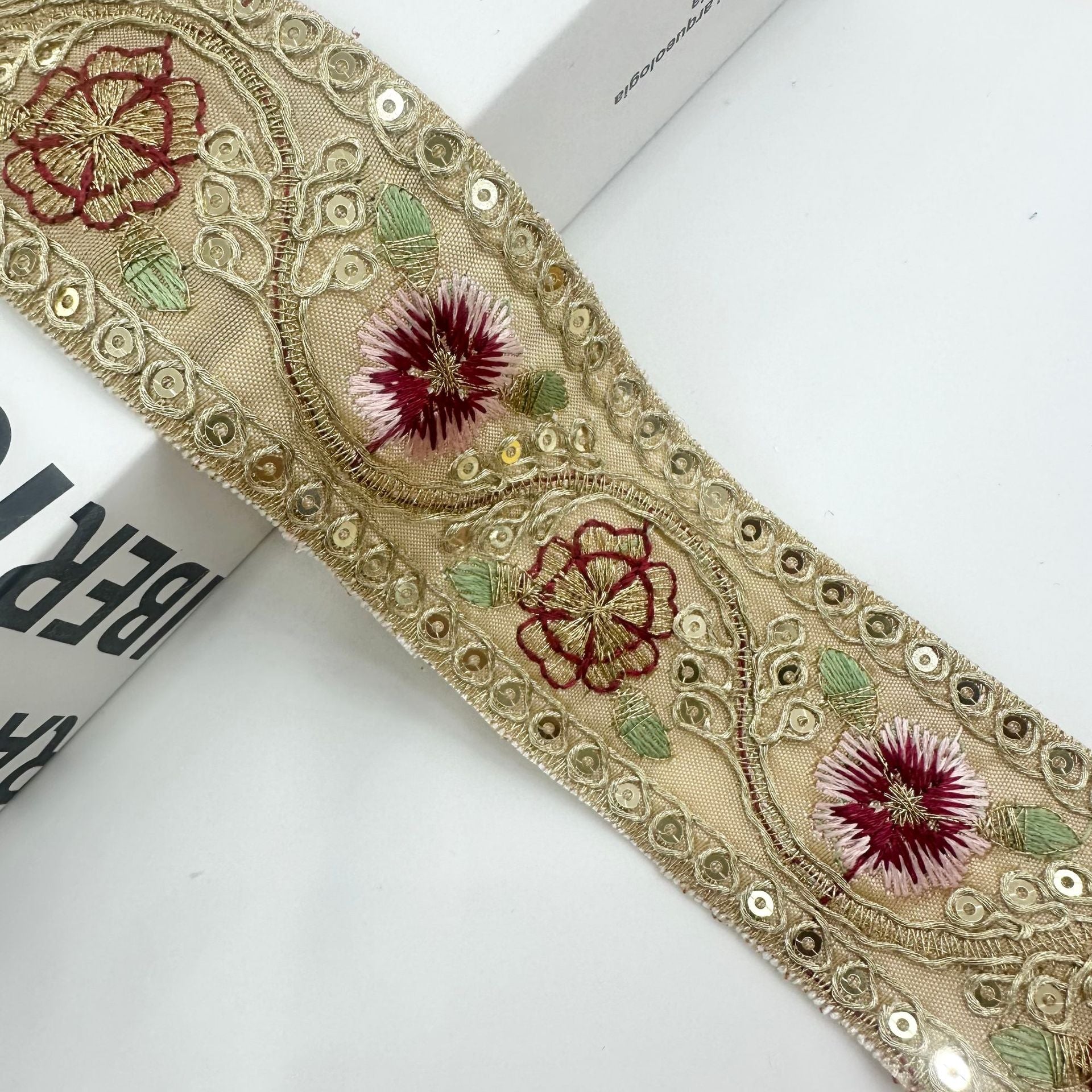 Beiger Kordeltrim mit roter Blüte, burgunder Rankenmuster und grünen Blättern
