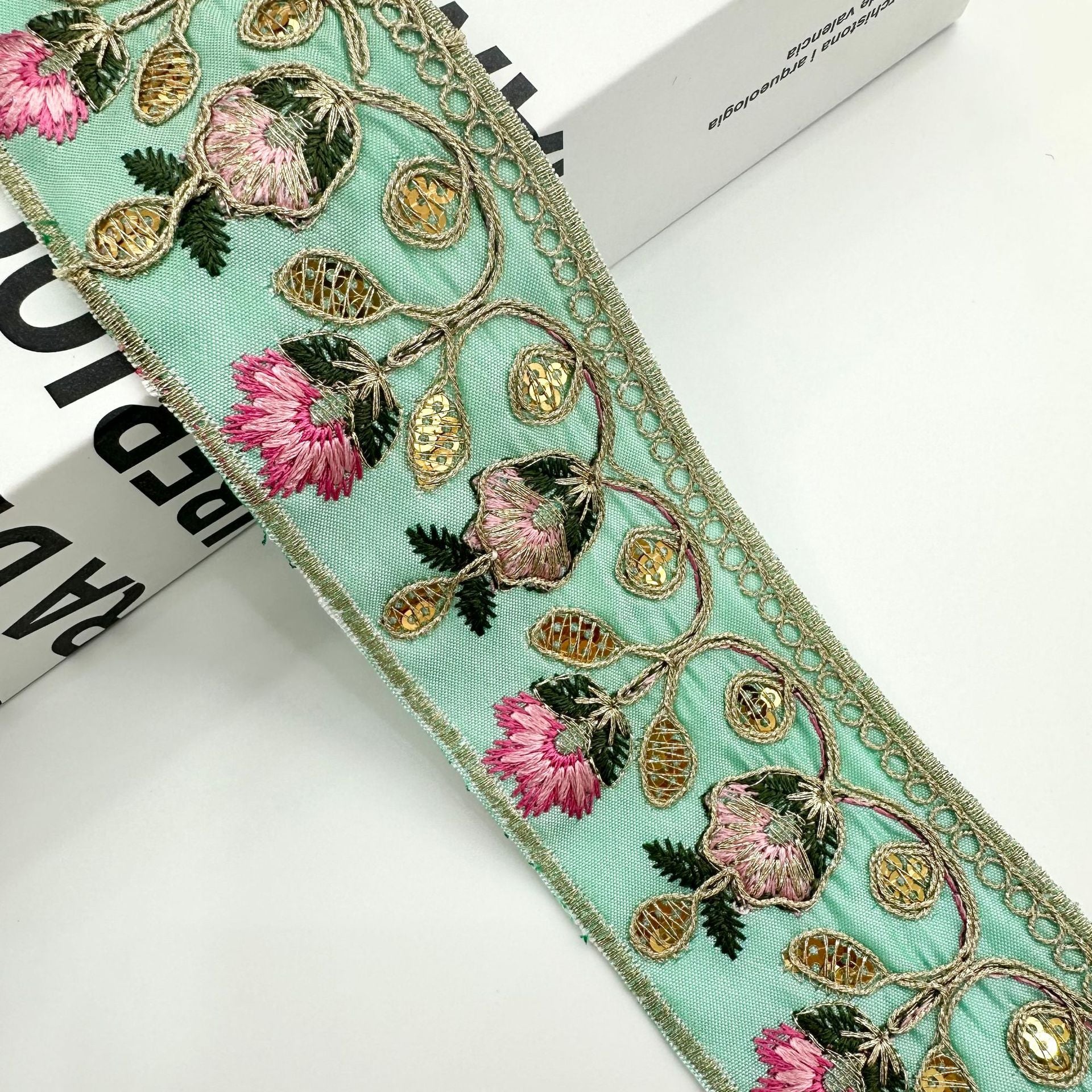 Teal embroidered lace trim ribbon with pink pom-pom flowers, gold loops, and scalloped edge