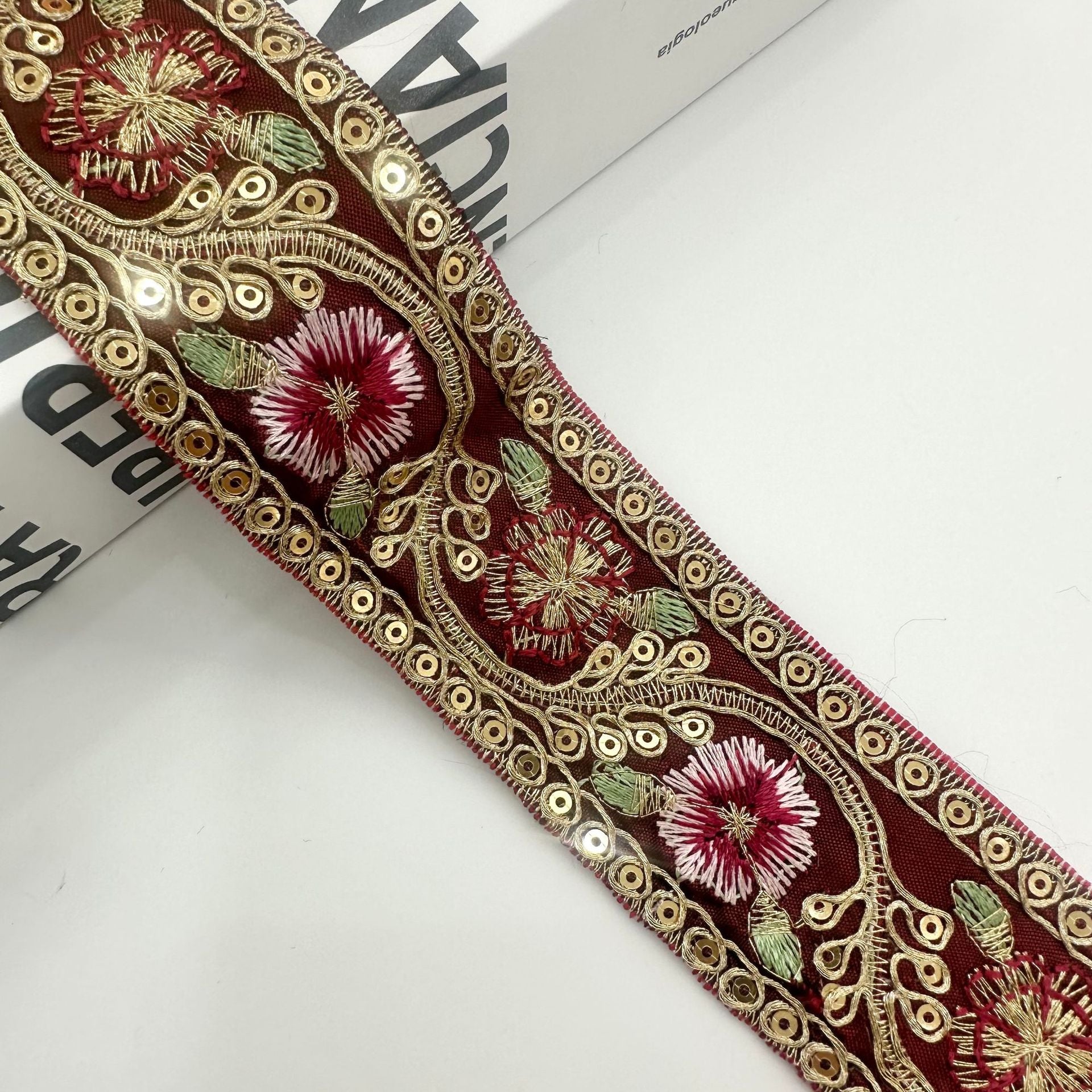 Grüner bestickter Besatz mit roter Blüte, rotem Blumenmuster und goldenen Ösen