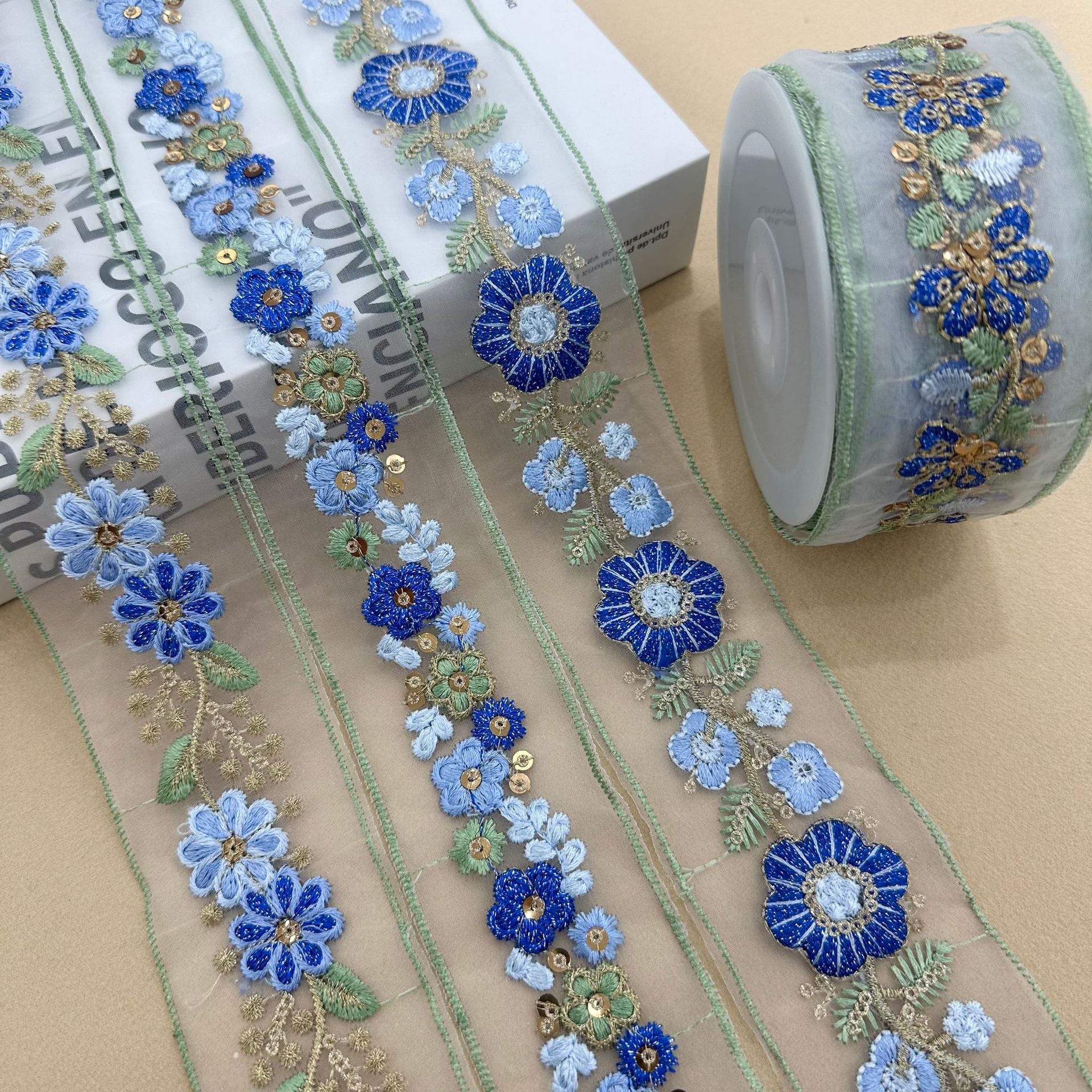 Aufgerolltes blaues Organza-Spitzenband mit floralen Paillettenstickereien, goldene Akzente