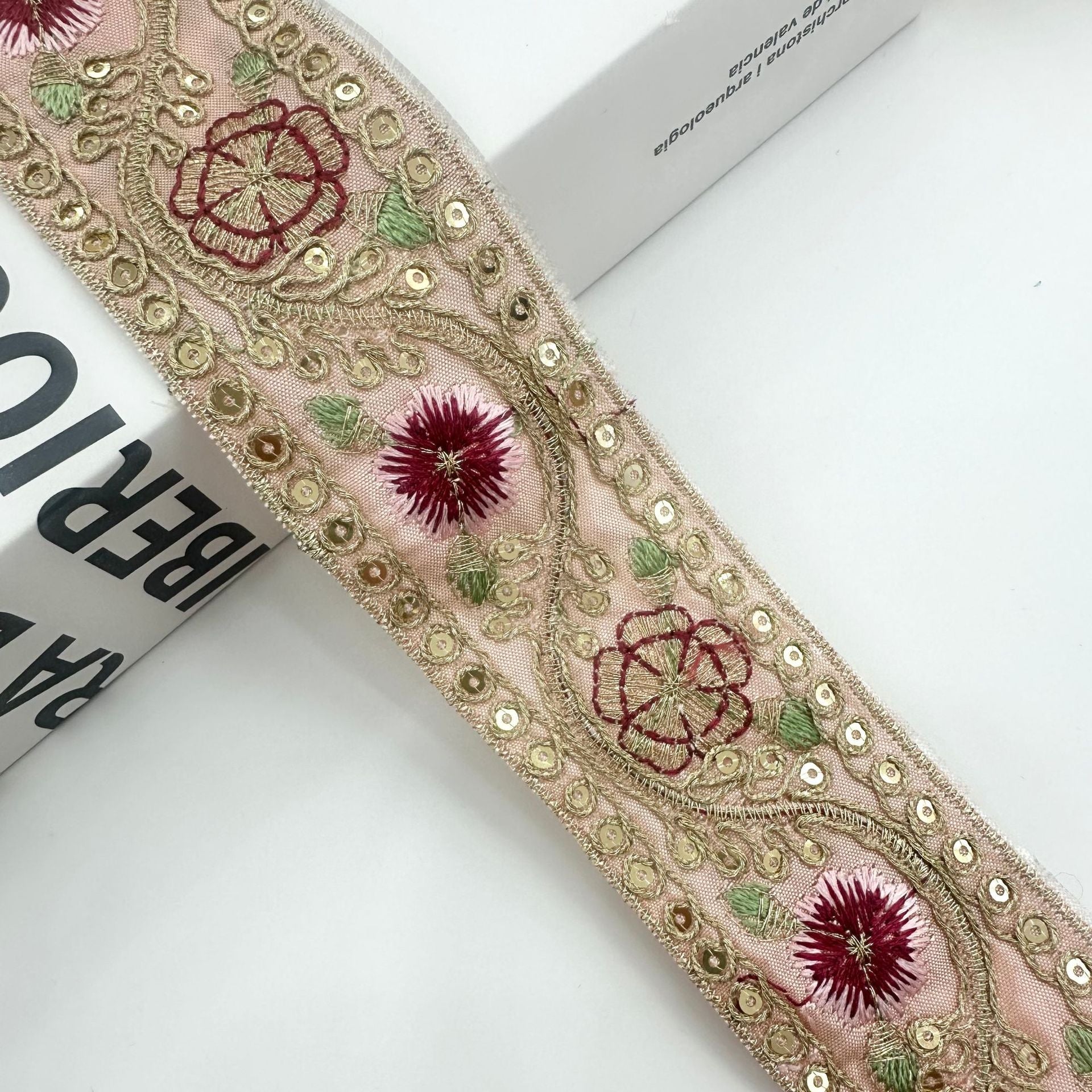 Heller rosé-beiger bestickter Besatz mit roten Blüten, rotem Rankenmuster und grünen Blättern