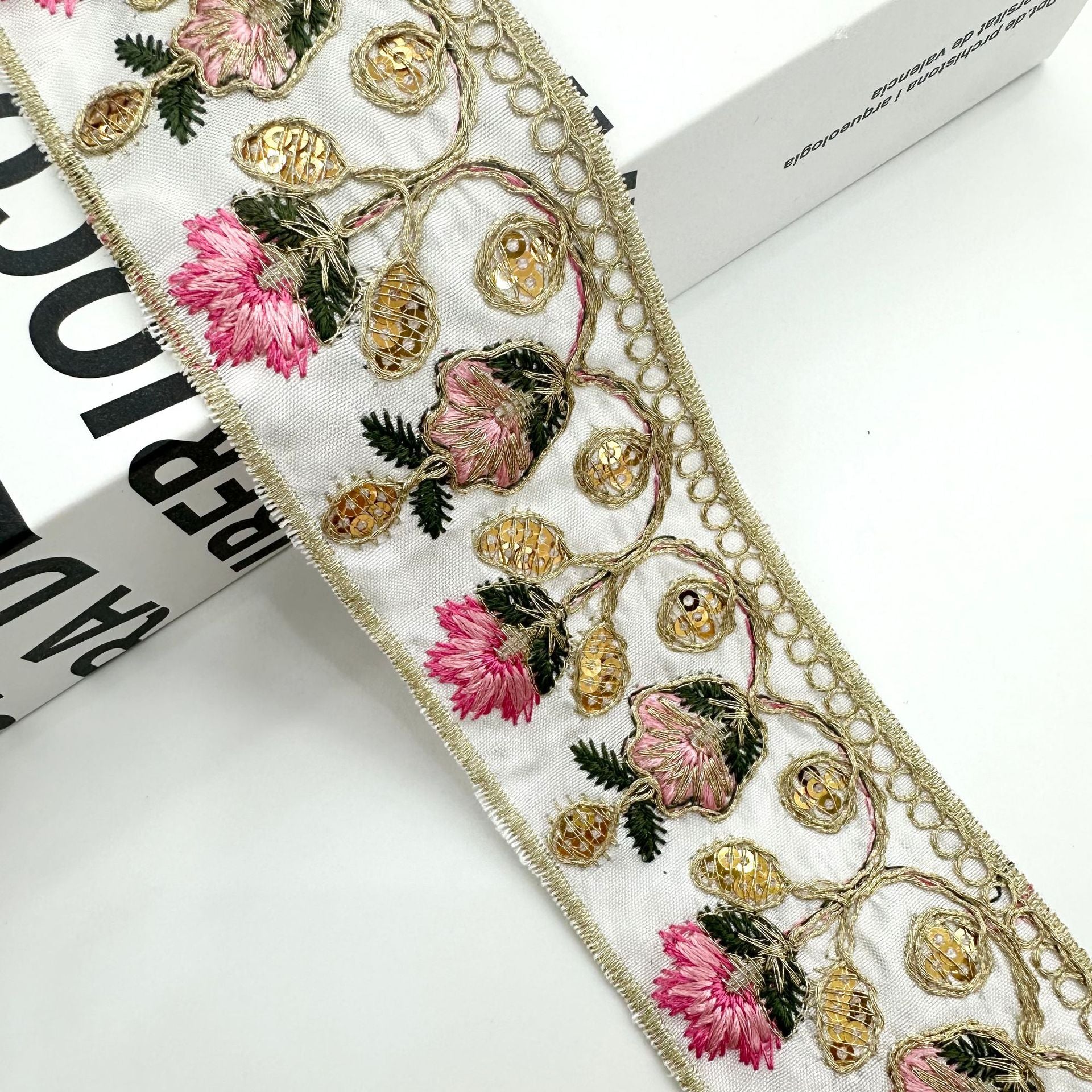 White embroidered lace trim ribbon with gold motifs and pink flowers along the border