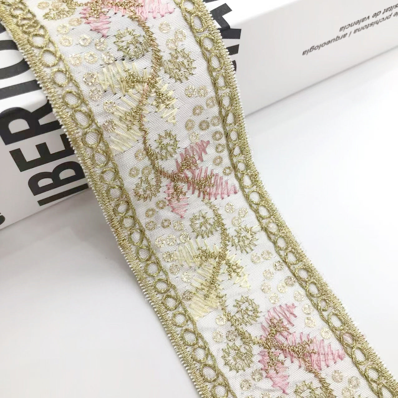 Close-up of sequin embroidered border ribbon with gold loops and pink-gold flowers